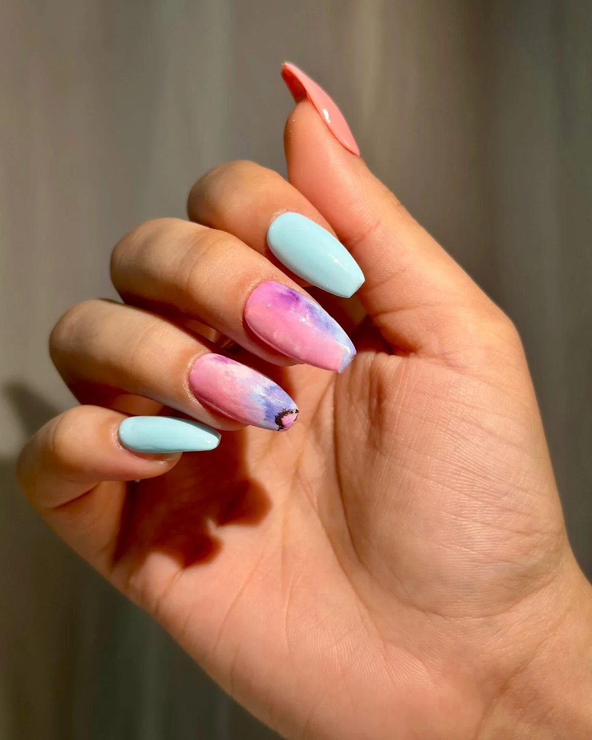 Custom coral, blue and painted press-on nails worn on a hand